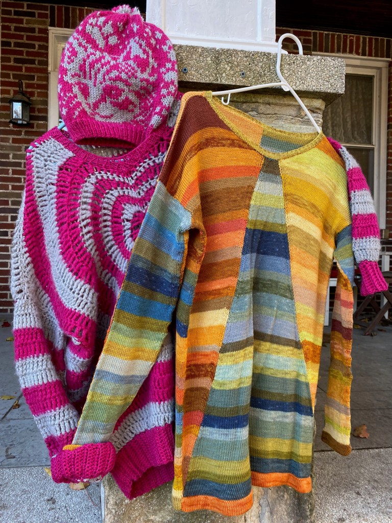 Crocheted heart sweater and knitted hat with kitten faces posed with paneled machine-knit pullover knitted from plant-dyed yarn, front view