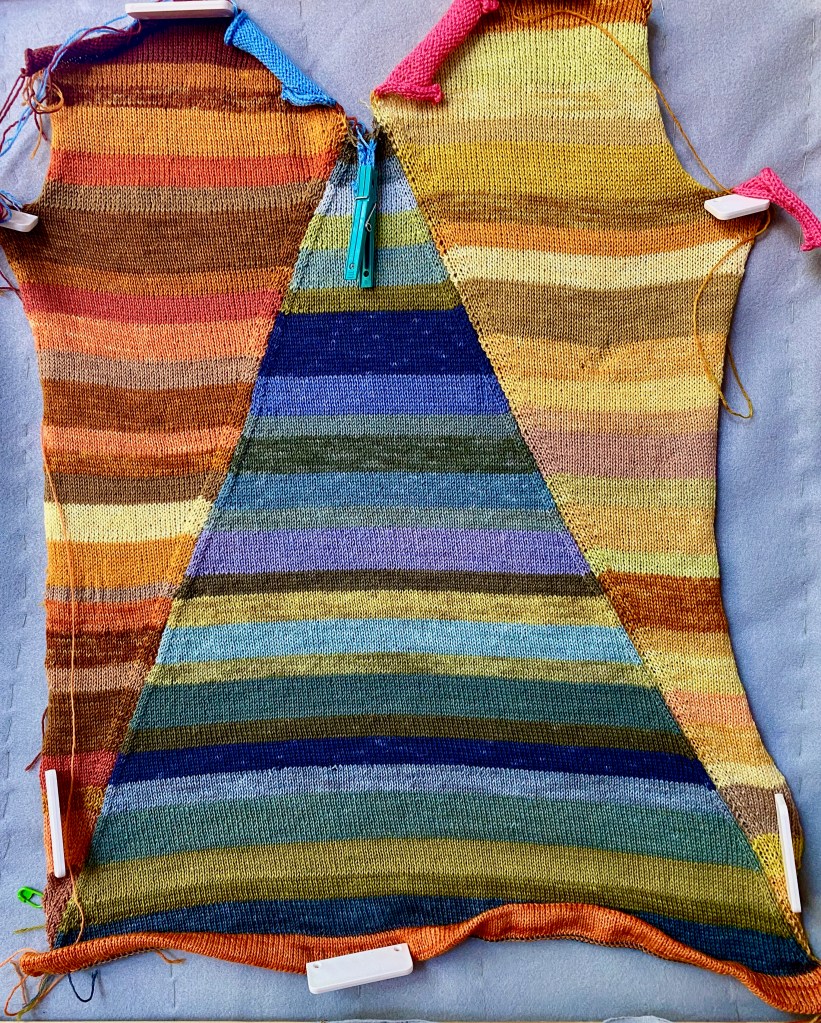 Front of machine-knit sweater knitted in shaped panels of plant-dyed yarn with a blue striped triangle in the center and an orange striped panel and a yellow striped panel on either side