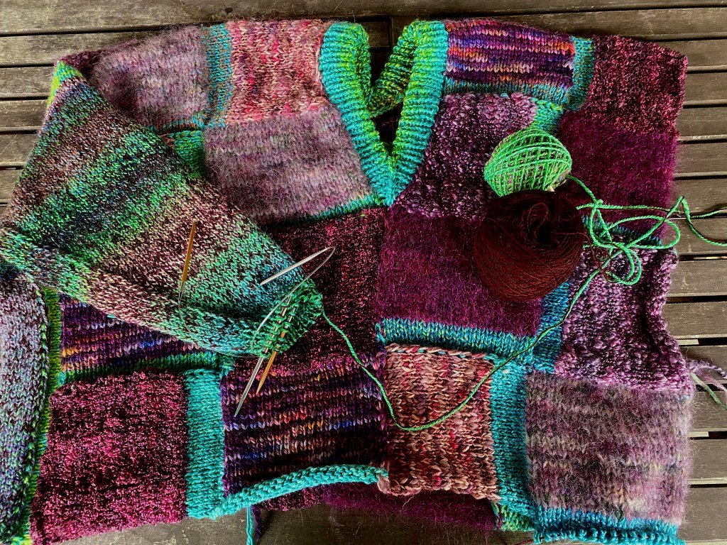 Modular patchwork pullover with deep V neck and side panel that connects front and back, leading up to a mostly knitted sleeve