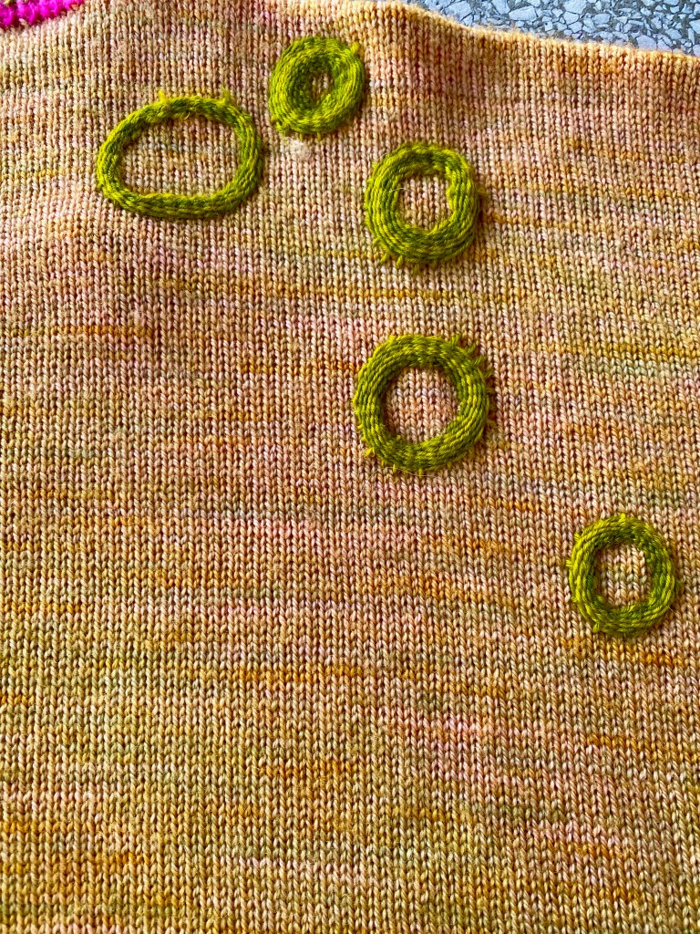 Embroidered green rings on discolored knitting