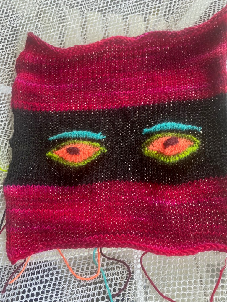 Patch pocket with machine-knit eyes against a wide strip of black.