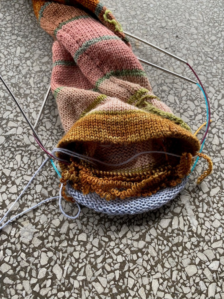 Inside of frayed cuff with new knitting on needle on the outside. Stitches on the inside of the cuff are on a second needle