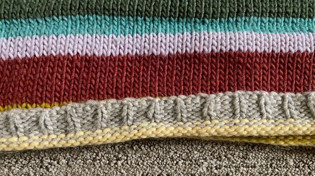 Detail of bottom hem, with pale yellow reverse stockinette below hand-manipulated ribbing in heather gray
