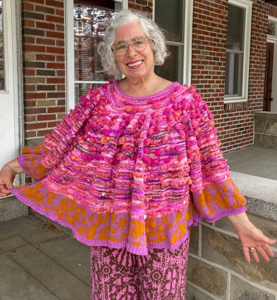 Swoncho top modeled with one side of hem held out to show improvised stranded patterning and embroidered bullions